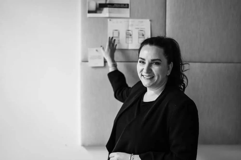 Schwarz weiß Foto von Julia Sahm, wie sie anhand einiger angepinnter Beispielbilder auf einer Wand etwas erklärt.