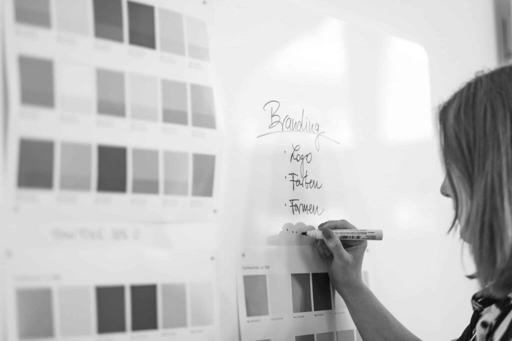 Schwarz weiß Fotografie von einer Frau die wichtige Stichpunke zum Thema Branding und Corporate-Design an ein Whiteboard schreibt.