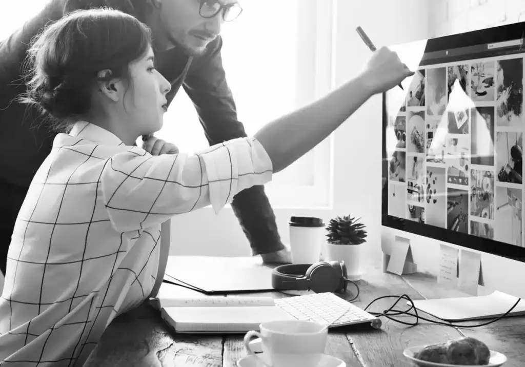 Zwei Personen arbeiten gemeinsam eine Webseitenastrategie anhand einiger Bilder am PC aus.
